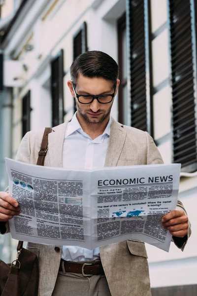 Visão frontal de homem concentrado em óculos lendo jornal na rua — Fotografia de Stock