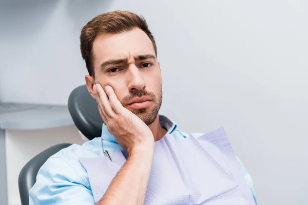 Chateado barbudo homem tocando rosto enquanto tendo dor de dente na clínica dentária — Fotografia de Stock