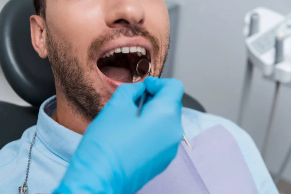 Vista ritagliata del dentista che tiene lo specchio dentale in bocca del paziente barbuto — Foto stock