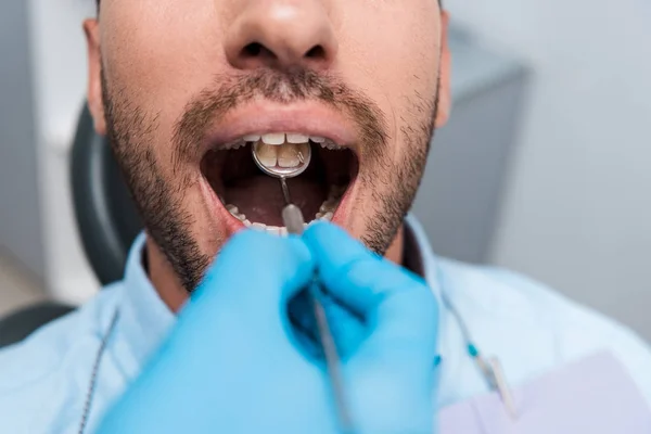 Vista recortada del dentista que sostiene el espejo dental en la boca del paciente - foto de stock