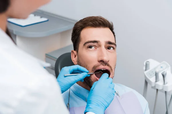 Foco seletivo do homem barbudo olhando para o dentista segurando equipamentos odontológicos — Fotografia de Stock
