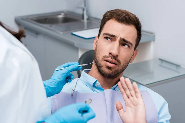 Enfoque selectivo del gesto paciente barbudo cerca de la mujer sosteniendo instrumentos dentales - foto de stock