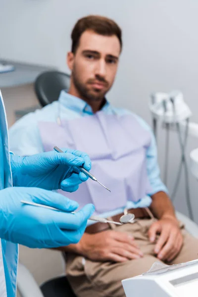 Selektiver Fokus des Zahnarztes in blauen Latexhandschuhen, die zahnärztliche Instrumente in der Nähe des Menschen halten — Stockfoto