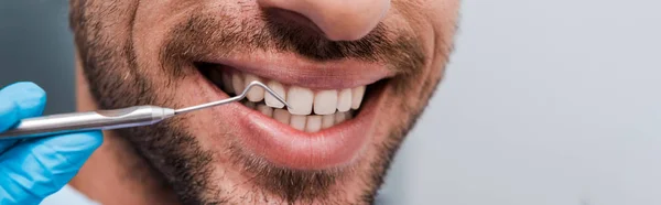 Panoramaaufnahme eines Zahnarztes, der ein zahnärztliches Instrument in der Nähe eines fröhlichen Mannes hält — Stockfoto