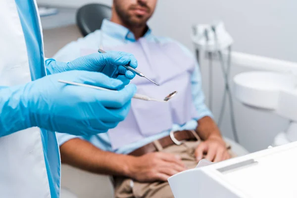 Messa a fuoco selettiva del dentista in guanti di lattice blu con strumenti dentali vicino al paziente — Stock Photo