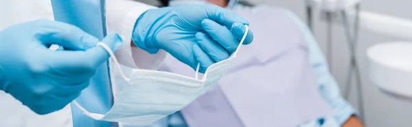 Panoramic shot of dentist holding medical mask in dental clinic — Stock Photo