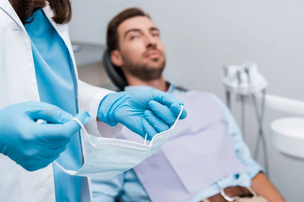 Vista ritagliata del dentista che tiene maschera medica vicino al paziente in clinica dentale — Foto stock