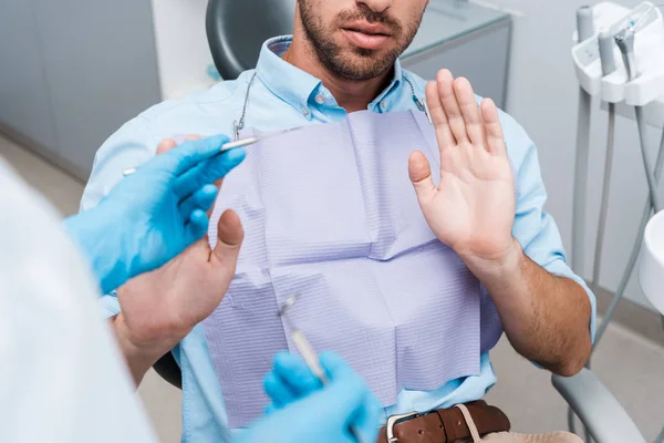 Селективное внимание человека жестикулируя рядом стоматолога, держащего стоматологические инструменты — стоковое фото