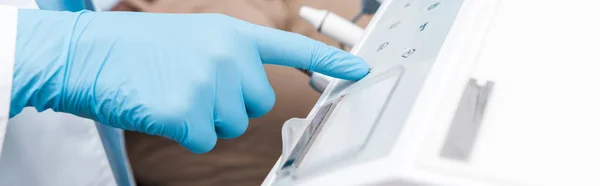 Panoramic shot of dentist in blue latex glove pointing with finger at dental equipment — Stock Photo