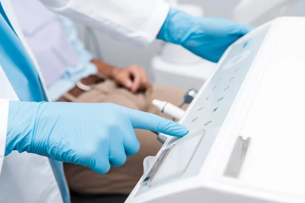 Cropped view of dentist in blue latex glove pointing with finger at dental equipment — Stock Photo