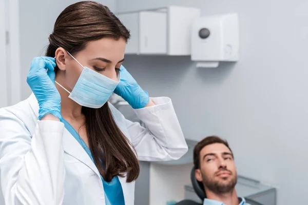 Selective focus of dentist in latex gloves touching medical mask near patient — Stock Photo