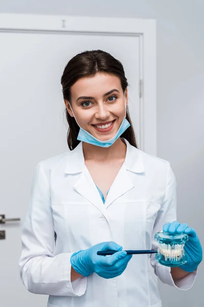 Cheerful dentist in medical mask holding pen near teeth model — Stock Photo