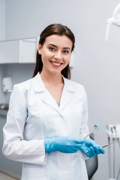 Dentista feliz em luvas de látex azul segurando instrumentos médicos inoxidáveis — Fotografia de Stock