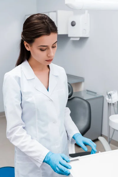Atractivo dentista en guantes de látex azul señalando con el dedo en la clínica - foto de stock