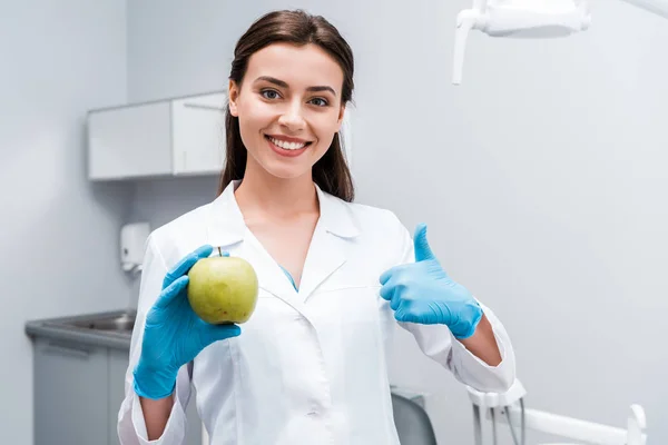 Веселий стоматолог тримає яблуко і показує великий палець в клініці — стокове фото