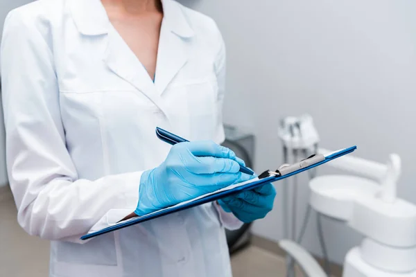 Cropped view of dentist writing while holding clipboard in clinic — Stock Photo