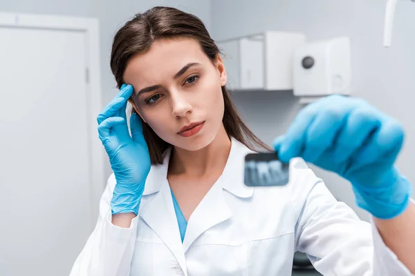 Selective focus of pensive and attractive dentist looking at x-ray — Stock Photo