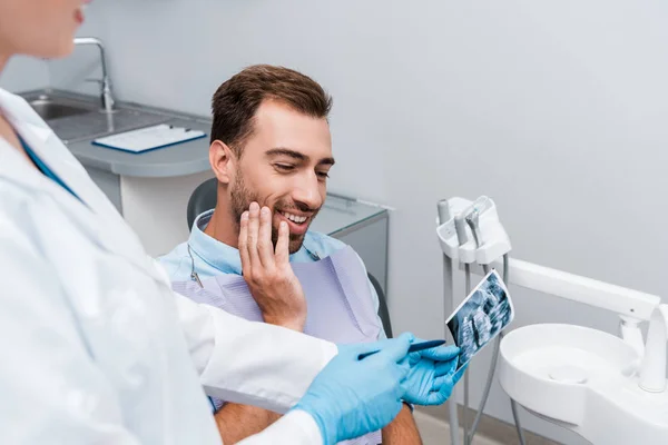 Селективное внимание веселого человека, смотрящего на рентген рядом с стоматологом в белом халате — стоковое фото
