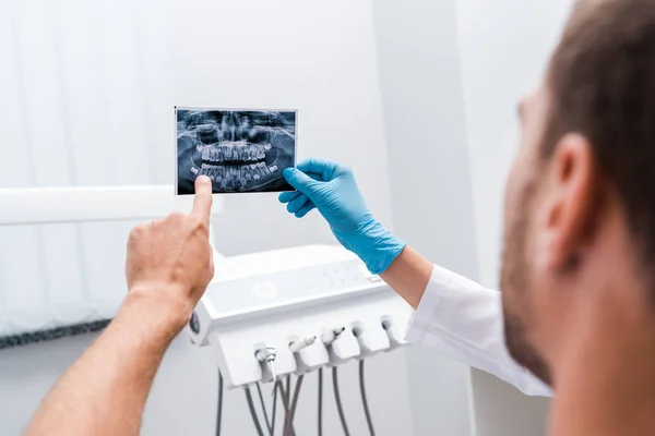 Visão recortada do dentista segurando raio-x perto do paciente apontando com o dedo na clínica — Fotografia de Stock