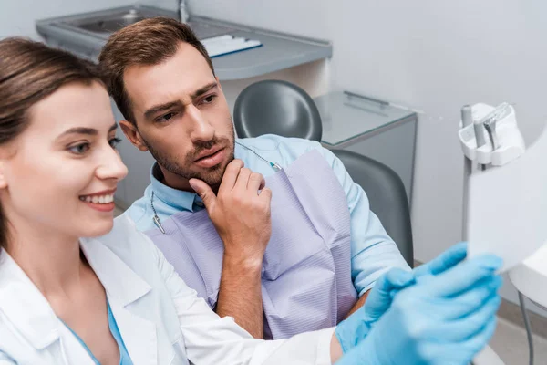 Enfoque selectivo del hombre guapo cerca del dentista sonriendo en la clínica - foto de stock