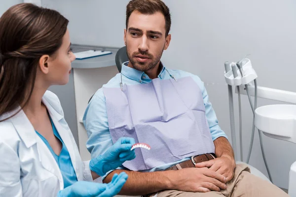 Messa a fuoco selettiva del paziente seduto vicino al dentista con modello di denti in clinica — Foto stock