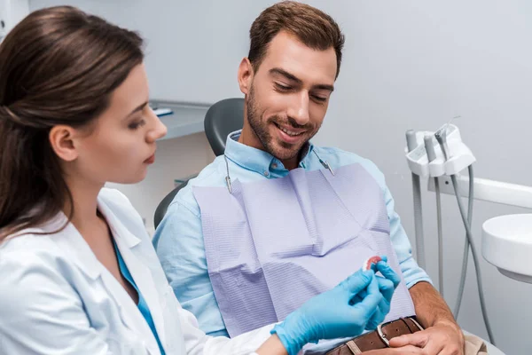 Selective focus of cheerful patient sitting near dentist and looking at teeth model in clinic — Stock Photo