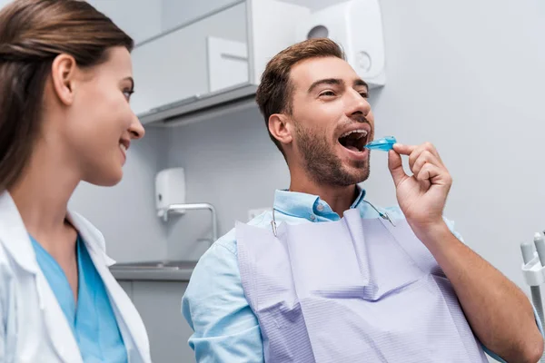 Foyer sélectif du patient mettre le dispositif de retenue dans la bouche près du dentiste heureux — Photo de stock