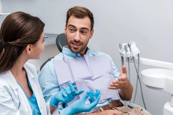 Selective focus of bearded man gesturing near woman holding retainer in clinic — Stock Photo