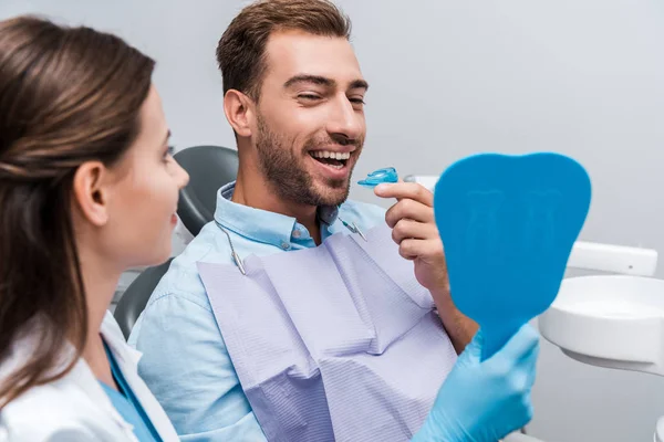 Selective focus of happy man looking at mirror and holding retainer near woman — Stock Photo