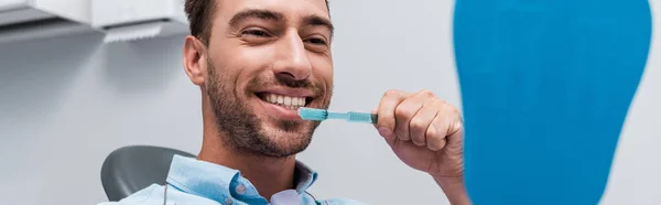 Panoramic shot of cheerful man looking at mirror and brushing teeth — Stock Photo