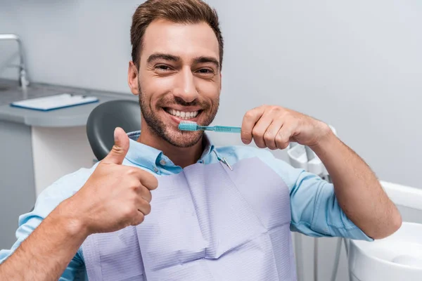 Hombre barbudo guapo mostrando el pulgar hacia arriba mientras sostiene el cepillo de dientes - foto de stock