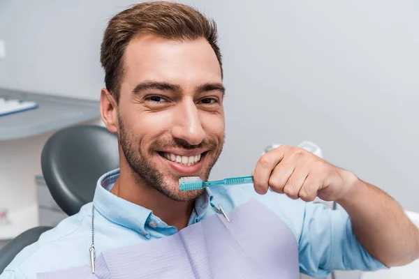 Hombre barbudo feliz mirando a la cámara y sosteniendo el cepillo de dientes - foto de stock