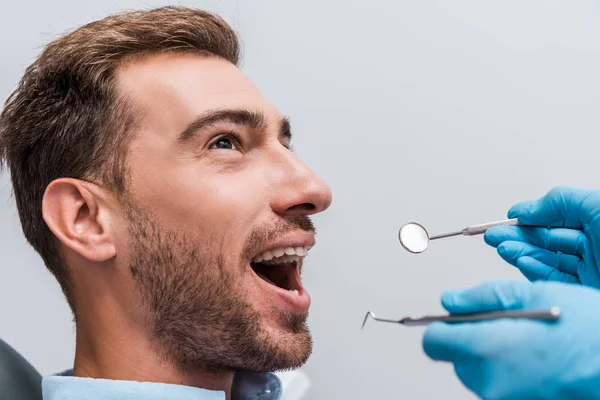 Cropped view of woman in latex gloves holding dental instruments near handsome bearded man — Stock Photo