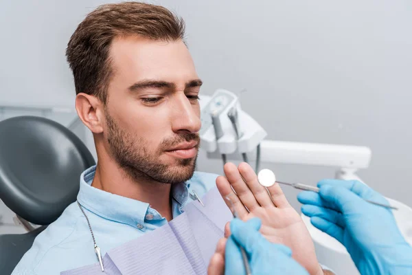 Обрезанный взгляд стоматолога в латексных перчатках, держащих стоматологические инструменты рядом с жестом пациента в клинике — стоковое фото