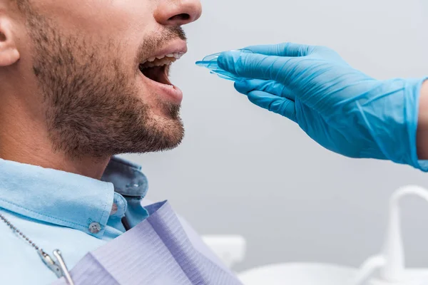 Cropped view of dentist in latex glove holding retainer near man with opened mouth — Stock Photo