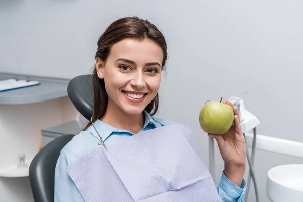 Весела жінка посміхається і тримає зелене смачне яблуко — стокове фото
