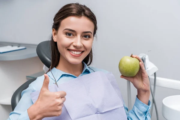 Mujer alegre sosteniendo manzana verde y sabrosa mientras muestra el pulgar hacia arriba - foto de stock