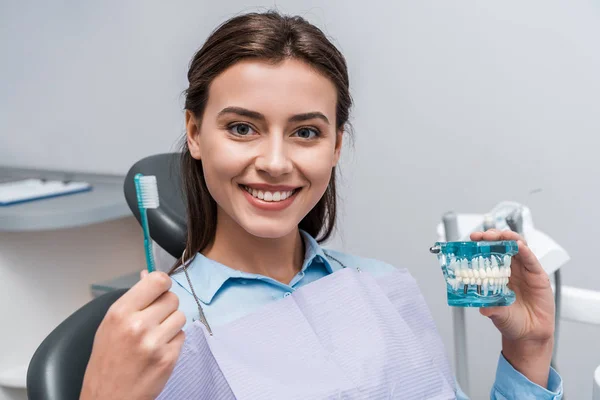 Happy woman holding toothbrush and teeth model in dental clinic — Stock Photo