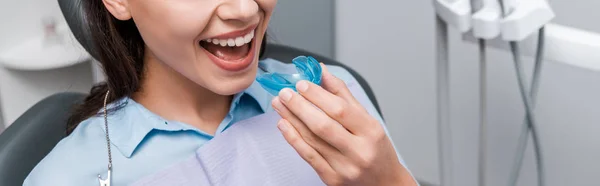 Panoramic shot of woman holding blue retainer in dental clinic — Stock Photo