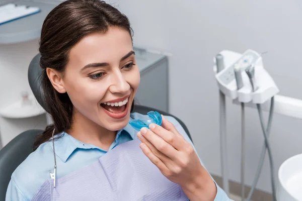 Mulher feliz segurando retentor azul e sorrindo na clínica odontológica — Fotografia de Stock