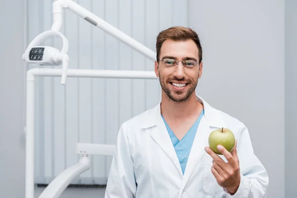 Happy bearded doctor in glasses holding green and tasty apple — Stock Photo