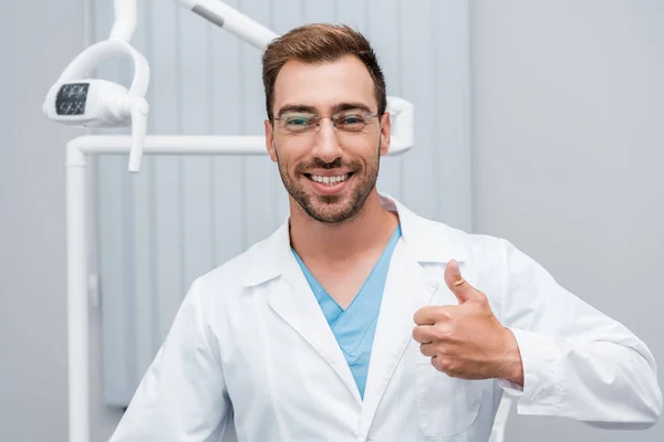 Felice medico in occhiali mostrando pollice in clinica — Foto stock