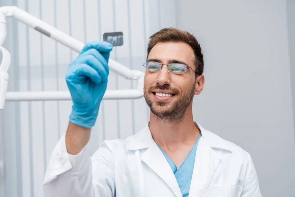 Selektiver Fokus des gut gelaunten Zahnarztes in Brille mit Röntgenbild in der Klinik — Stockfoto