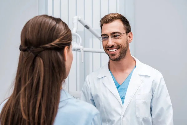 Enfoque selectivo del dentista alegre en gafas mirando al paciente en la clínica - foto de stock