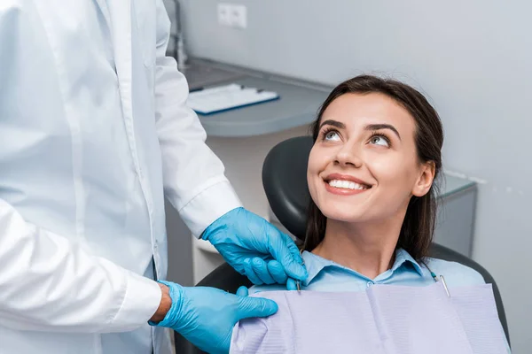 Vista recortada del dentista en guantes de látex cerca de la mujer alegre - foto de stock