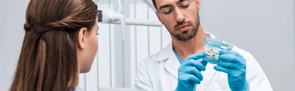 Panoramic shot of dentist holding tooth model near woman — Stock Photo