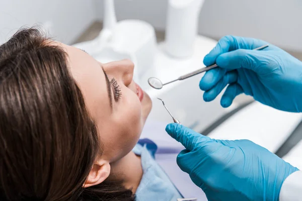 Vista recortada del hombre en guantes de látex que sostienen instrumentos dentales cerca de mujer atractiva - foto de stock