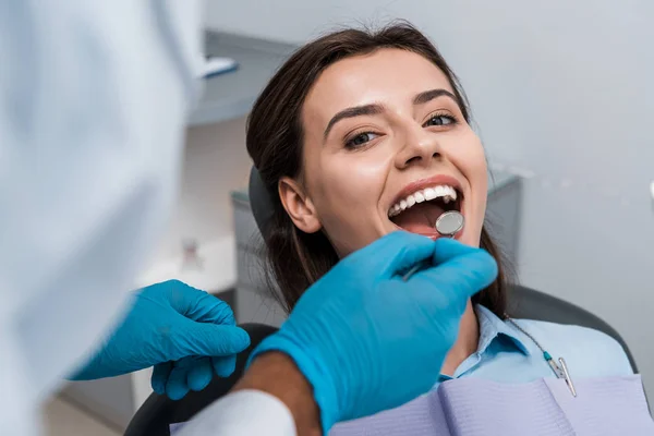 Selective focus of dentist in latex gloves holding dental mirror near woman — Stock Photo