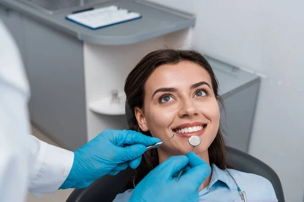 Foco seletivo do homem em luvas de látex segurando instrumentos dentários perto de mulher positiva — Fotografia de Stock