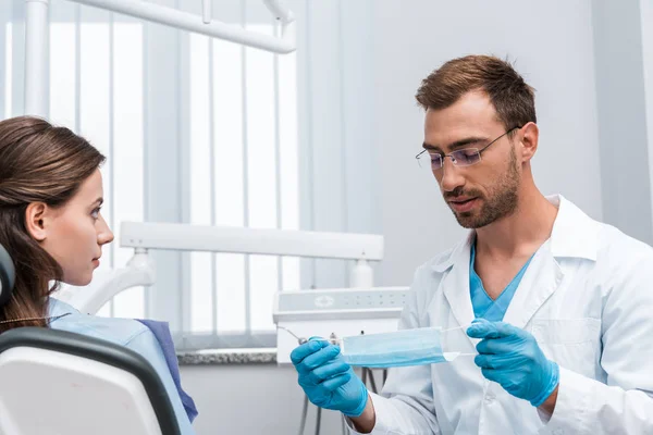 Selektiver Fokus eines gutaussehenden Mannes in Brille mit medizinischer Maske in der Nähe eines attraktiven Patienten — Stockfoto